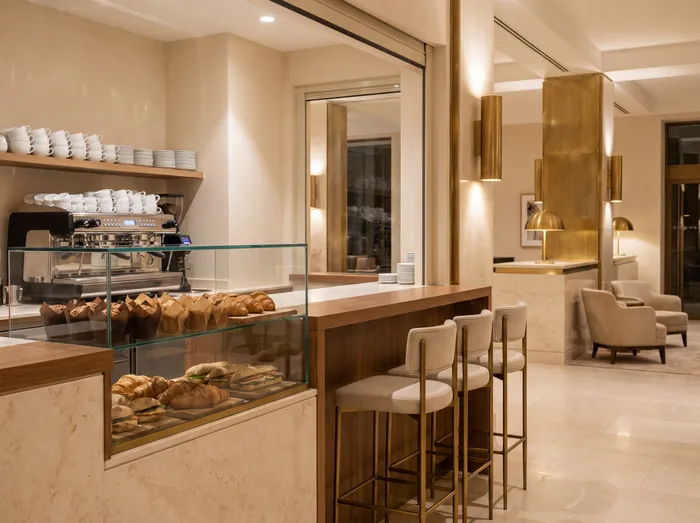 A lobby café counter with an espresso machine and a glass case of muffins and wrapped sandwiches